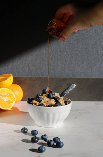 istock hand adding honey on oatmeal with blueberries on top in white porcelain bowl 1470802073