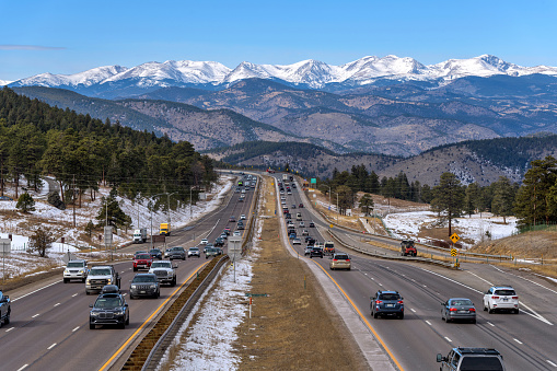 Denver, Colorado, USA - November 23, 2022: A sunny Winter day view of busy Interstate Highway I-70, with snow-capped high peaks of Continental Divide towering at west.