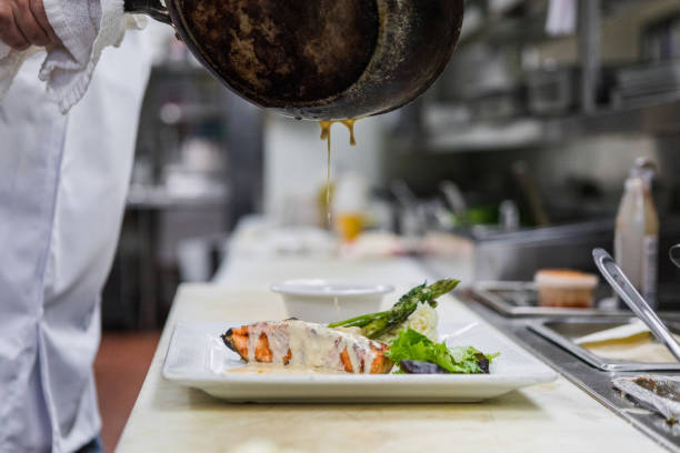 Unrecognizeable chef uses a skillet to pour sauce on the entree