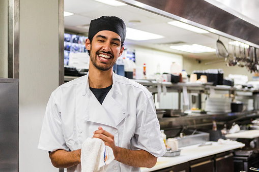 The male chef smiles proudly while having his photo taken in the kitchen at the restaurant.