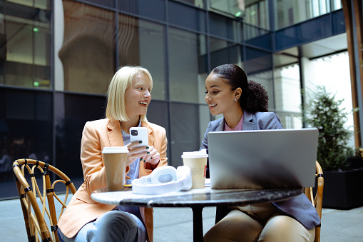 Two cheerful young women sitting at the table and discussing work