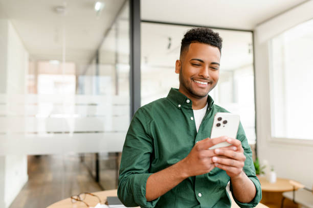 un jeune employé indien, pigiste, homme d’affaires se tient avec un smartphone à la main - téléphone mobile photos et images de collection