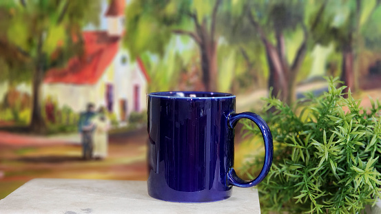 Blue coffee mug in foreground.  Couple in background in soft focus.  Church or school building.  Reminiscent of times gone by.