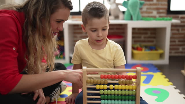 Teacher and toddler learning maths with abacus sitting on floor at kindergarten