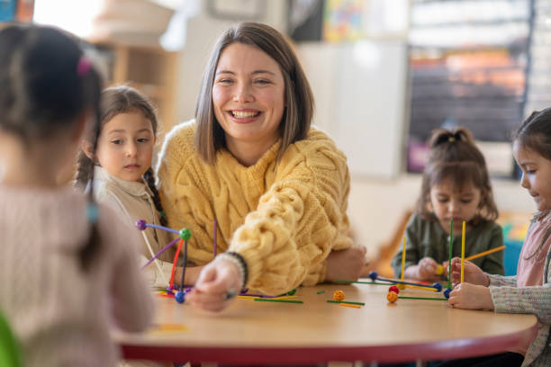 Kindergarten Students with Their Teacher A small group of Kindergarten students sit with their female teacher as they work away building structures. They are each dressed casually as they work on their projects and talk amongst themselves. preschool classroom jobs stock pictures, royalty-free photos & images
