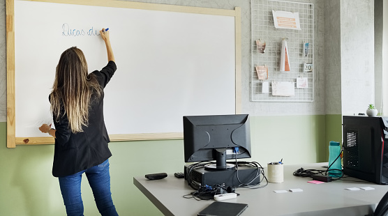Rear view of a female professor writing in portuguese on the whiteboard in classroom