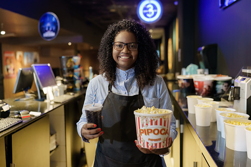 Portrait of cinema attendant looking at camera holding soda refills and popcorn.