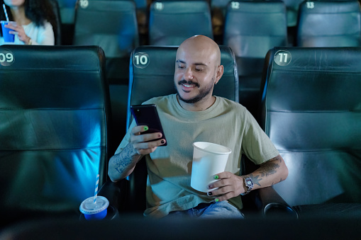 Man alone in movie theater texting on cell phone.