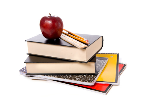 A stack of school books and spiral notebooks with a pencil and a ruler on top in front of a white background with an apple