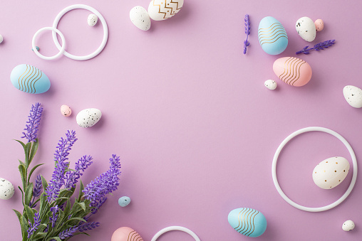 Easter decorations concept. Top view photo of white circles pink white blue easter eggs and lavender flowers on isolated pastel purple background with empty space in the middle