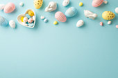 Easter decorations concept. Top view photo of colorful easter eggs heart shaped saucer with sweets and ceramic bunnies on isolated pastel blue background with copyspace