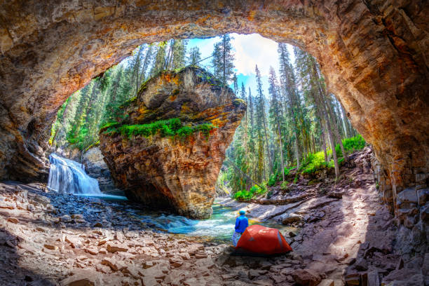 Hiker outside his camping tent at Hidden Cave with waterfall and limestone bedrock in Johnston Canyon at Banff National Park Hiker stands outside his camping tent at Hidden Cave with waterfall and limestone bedrock in Johnston Canyon at Banff National Park in the Canadian Rockies. johnston canyon banff, summer stock pictures, royalty-free photos & images