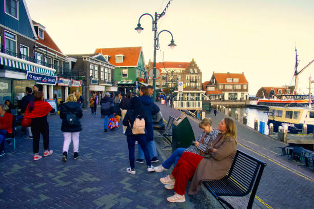 volendam, netherlands - 08 October 2022: people sitting on bench at harbor front of dutch village with souvenir shops and terraces