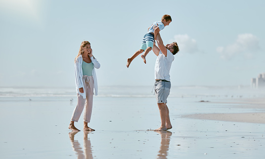 Family, beach and father lifting kid on vacation, holiday or summer trip outdoors. Love, support and care of mother, man and boy playing, bonding and having fun while enjoying quality time together