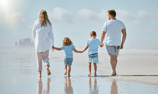 Family, beach and holding hands while walking in water on summer vacation with parents and children together for love, trust and support. Man, woman and kids at sea for a walk while on travel holiday