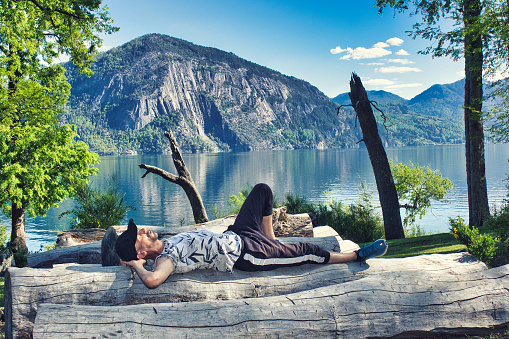 Relaxed tourist resting on vacation on logs in front of lake with mountains. High quality photo