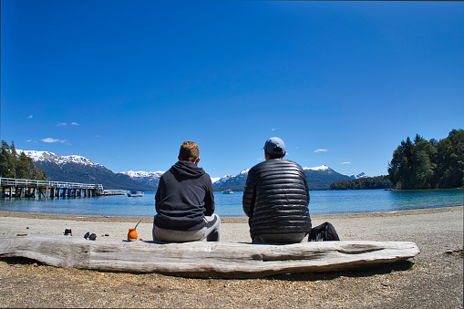 two men on their backs sitting on a log looking out over the lake