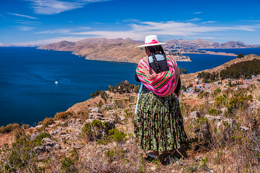 Aymara woman admiring view from Isla del Sol (Island Of The Sun), Lake Titicaca, Bolivia. Isla del Sol is an island in the southern part of Lake Titicaca. It is part of the modern Plurinational State of Bolivia. Geographically, the terrain is harsh; it is a rocky, hilly island. There are no motor vehicles or paved roads on the island. The main economic activity of the approximately 800 families on the island is farming, with fishing and tourism augmenting the subsistence economy. Of the several villages, Yumani and Cha'llapampa are the largest.There are over 80 ruins on the island. Most of these date to the Inca period circa the 15h century AD. Archaeologists have discovered evidence that people lived on the island as far back as the third millennium BCE. Many hills on the island contain agricultural terraces, which adapt steep and rocky terrain to agriculture. Among the ruins on the island are the Sacred Rock, a labyrinth-like building called Chicana, Kasa Pata, and Pilco Kaima. In the religion of the Incas, it was believed that the sun god was born here.