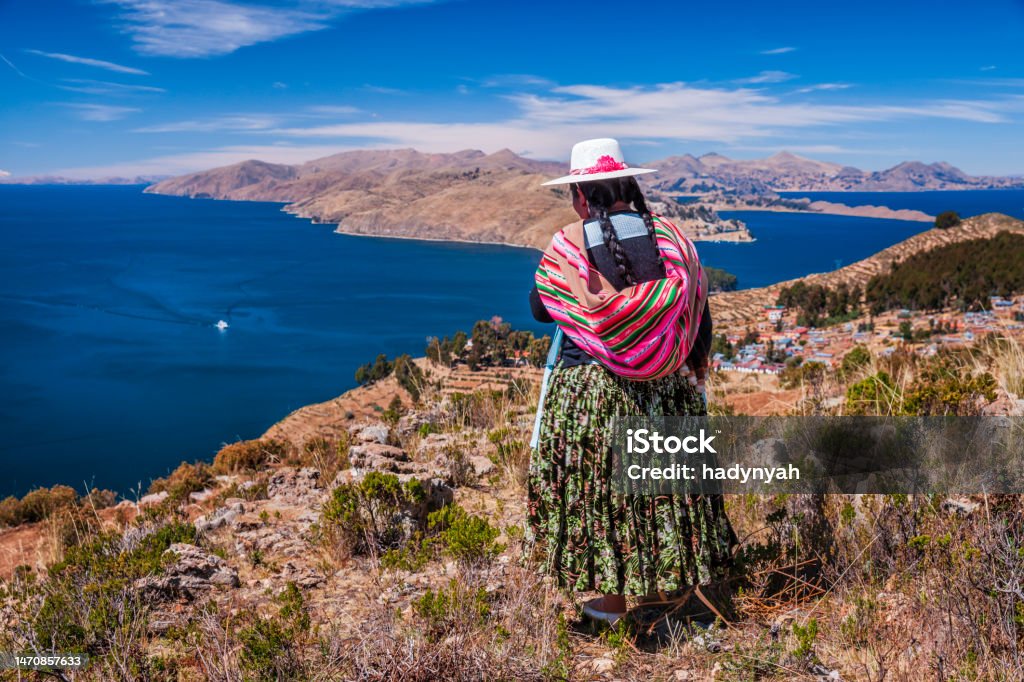 Aymara woman looking at view, Isla del Sol, Lake Titicaca, Bolivia Aymara woman admiring view from Isla del Sol (Island Of The Sun), Lake Titicaca, Bolivia. Isla del Sol is an island in the southern part of Lake Titicaca. It is part of the modern Plurinational State of Bolivia. Geographically, the terrain is harsh; it is a rocky, hilly island. There are no motor vehicles or paved roads on the island. The main economic activity of the approximately 800 families on the island is farming, with fishing and tourism augmenting the subsistence economy. Of the several villages, Yumani and Cha'llapampa are the largest.There are over 80 ruins on the island. Most of these date to the Inca period circa the 15h century AD. Archaeologists have discovered evidence that people lived on the island as far back as the third millennium BCE. Many hills on the island contain agricultural terraces, which adapt steep and rocky terrain to agriculture. Among the ruins on the island are the Sacred Rock, a labyrinth-like building called Chicana, Kasa Pata, and Pilco Kaima. In the religion of the Incas, it was believed that the sun god was born here. Lake Titicaca Stock Photo