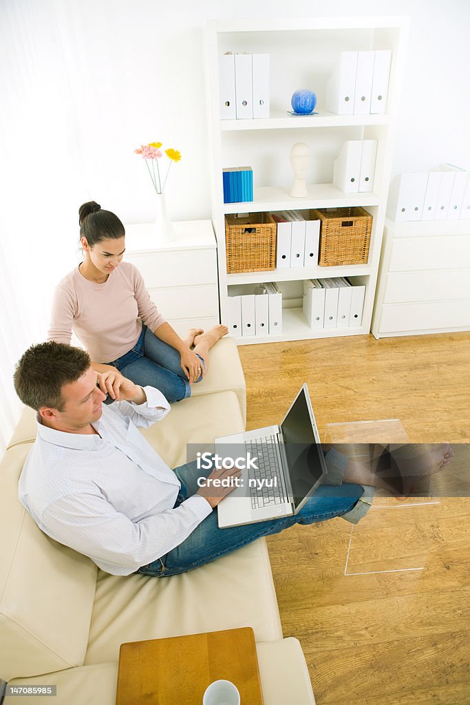 Working at home Couple sitting on couch at home, working on laptop, mobile phone in hand. Click here for other business images:  30-39 Years Stock Photo