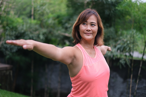 Shot of mature Asian woman practicing warrior pose in the garden outside her house.