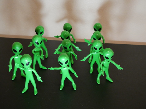 Several green aliens standing in different positions on a black surface. With black eyes and black mouth.