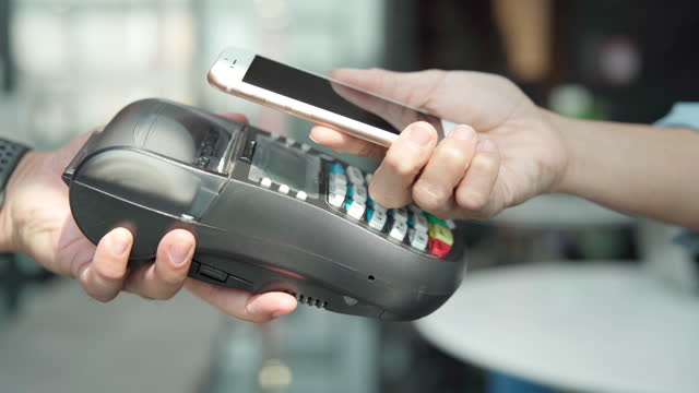 Asian people are using contactless payment by phone in a restaurant, hand with smartphone is touching payment terminal