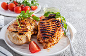 two juicy grilled chicken breasts on a white ceramic tray for serving with vegetables. front view. cement grey background. delicious food.