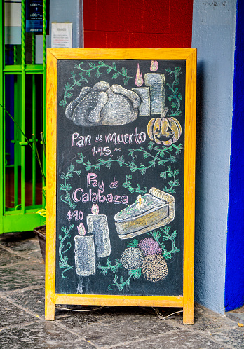 Coyoacan, Mexico City, Mexico - October 30, 2022: Day of the Dead signboard outside a restaurant in Coyoacan, Mexico City, Mexico. The sign advertises pumpkin pie and Day of the Dead bread.