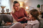 mother checking temperature on sick daughter laying in bed and gives syrup