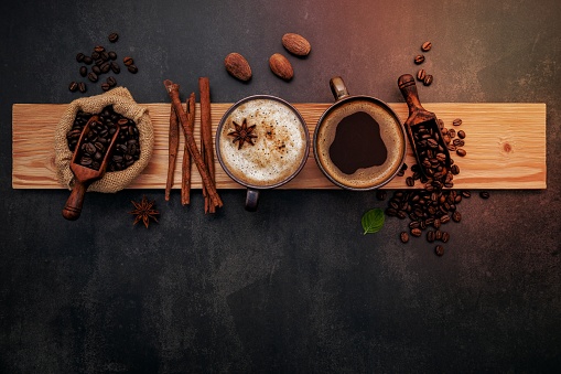 Roasted coffee beans with coffee powder and flavourful ingredients for make tasty coffee setup on dark stone background.