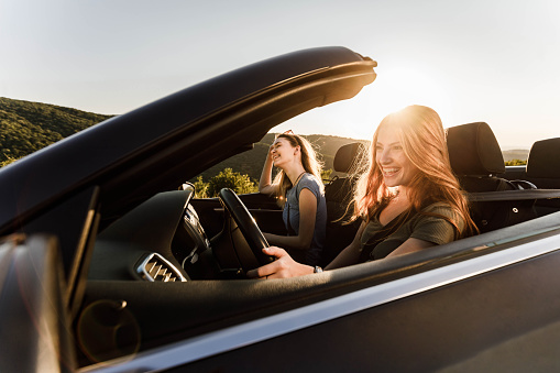 Cheerful female friends going on a road trip in convertible car.