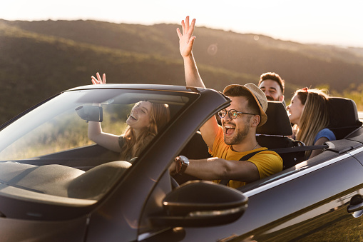 Group of happy friends having fun while going on a trip in a convertible car.