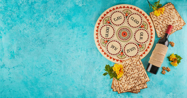 pesach celebration concept - jewish holiday pesach. background with yellow flowers with a glass of wine, matzah and a plate of seder on a blue background. traditional hebrew inscriptions on a plate. . - passover imagens e fotografias de stock