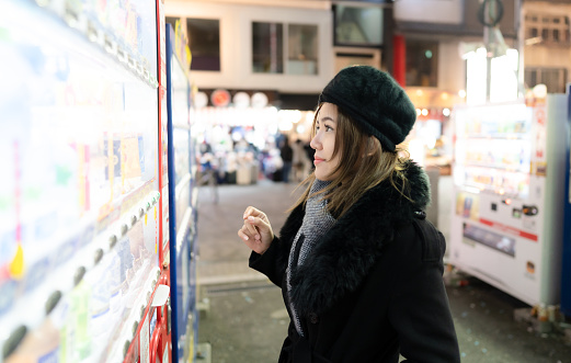 Woman tourist buying drinks from vending machine at market street night, Osaka city, Japan.