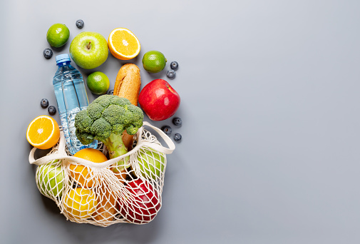 Shopping mesh bag full of healthy food on grey background. Flat lay with copy space