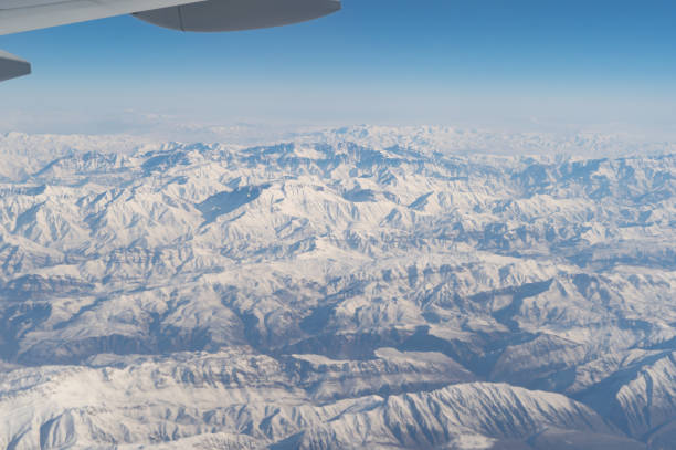 旅行と輸送のコンセプトで窓から雲の上を飛ぶ飛行機ジェットの航空写真の翼。冬の白い雪山。自然の風景の背景。 - mountain range earth sky airplane ストックフォトと画像