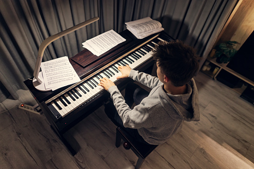 Teenage boy is practicing playing the piano in the living room at night. \nShot with Canon R5