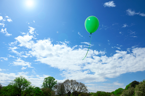 Green hot air balloon with basket and bird flock flying in the sky
