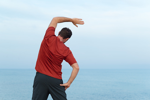 Rear view of a man stretching dorsal muscles while is looking at the sea.