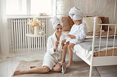 Morning routine. Caring mother and daughter in same bathrobes have fun and do manicure together after shower in hotel room