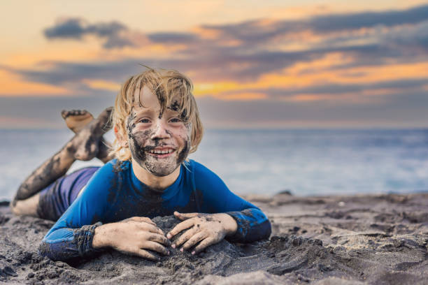 istock Black Friday concept. Smiling boy with dirty Black face sitting and playing on black sand beach. Summer vacation with kids. Black Friday, sales of tours and airline tickets or goods 1470893078
