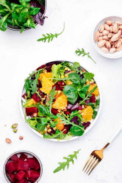 istock Beet and orange healthy salad with arugula, lamb lettuce, mini chard and pistachios, white kitchen table, copy space. Fresh useful vegan dish for healthy eating 1470895005