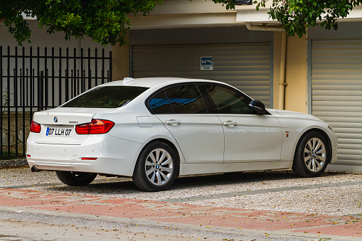 Side, Turkey -January 21, 2023:   white  BMW 3-series 320i  is parked  on the street in city against the backdrop of a buildung,  shops
