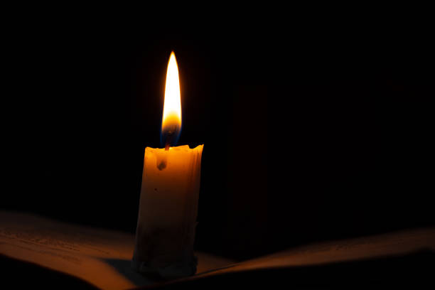 a burning candle stands on a book in a dark room