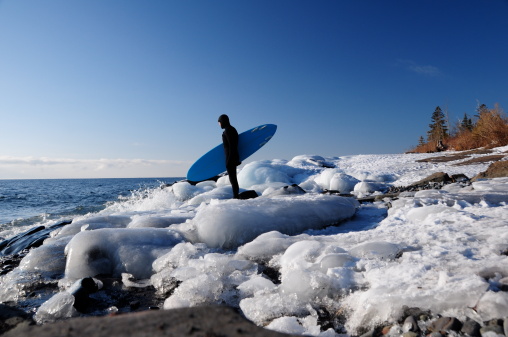A surfer contemplates the water in a wintry, icy, shoreline. Lake Superior, Minnesota, USA.