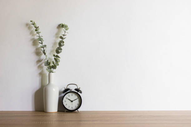 istock Green leaves on ceramic pot and clock on wooden table with natural light. 1470902657