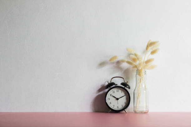 istock White flowers in a clear bottle and clock over pink table with natural light. 1470902705