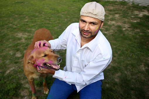 Pet owner celebrating Holi festival with his dog outdoors in the public park.