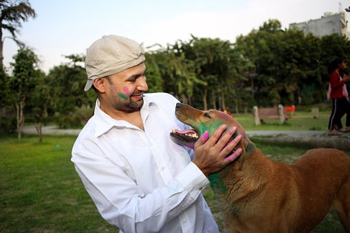 Pet owner celebrating Holi festival with his dog outdoors in the public park, Delhi, India.